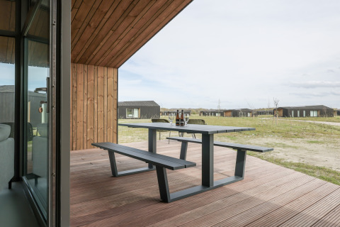 Udendørs terrasse med bænk og bord på Heerlijkheid Vlietenburg 1 lodge i Holland, udsigt til hytter.