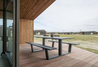 Udendørs terrasse med bænk og bord på Heerlijkheid Vlietenburg 1 lodge i Holland, udsigt til hytter.