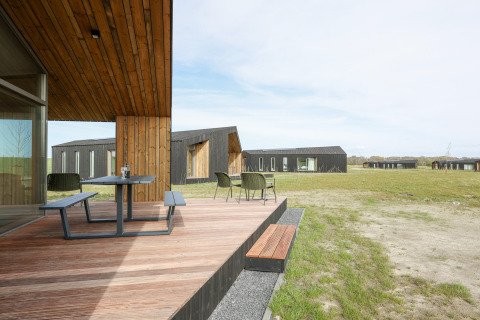 Træterrasse med bord og stole foran moderne lodges i grønne omgivelser på Heerlijkheid Vlietenburg 1, Holland.
