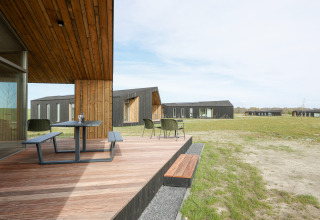 Træterrasse med bord og stole foran moderne lodges i grønne omgivelser på Heerlijkheid Vlietenburg 1, Holland.