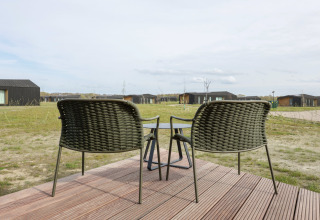 To flettede stole og et bord på en træterrasse med udsigt over Heerlijkheid Vlietenburg 1, Nederlandene.