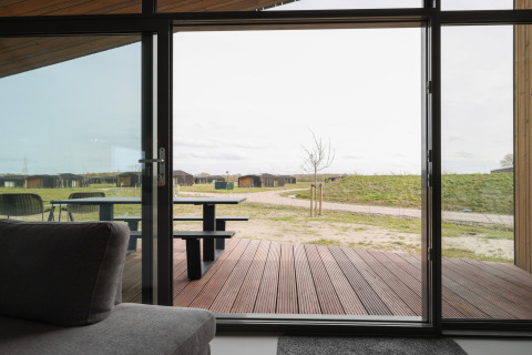 Udsigt fra en lodge med glasdør til terrasse og grønne områder i Heerlijkheid Vlietenburg, Holland.