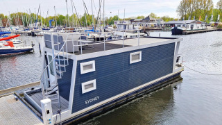 Woonboot Havenlodge N aangemeerd bij Marina Parcs Naarden in Nederland, omgeven door jachten en boten.