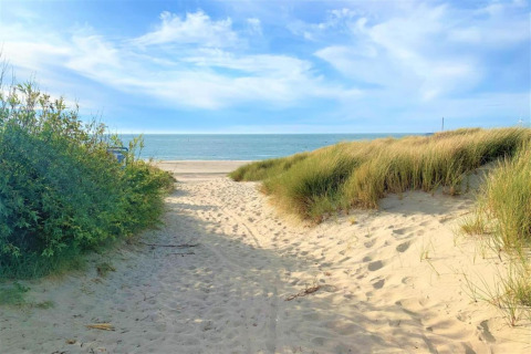Pathway through sand dunes at a glamping site, leading to the beach with blue sky and calm sea view.