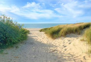 Sti gennem sandklitter ved glampingplads, med udsigt til stranden, himlen og havet i baggrunden.