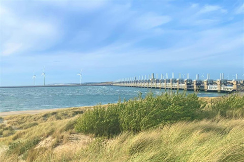 View of wind turbines and a dam by the sea, seen from the grass near a glamping accommodation area.