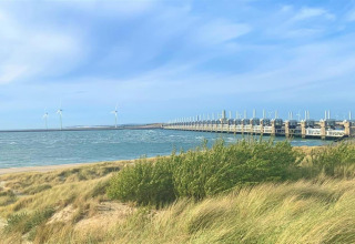 View of wind turbines and a dam by the sea, seen from the grass near a glamping accommodation area.
