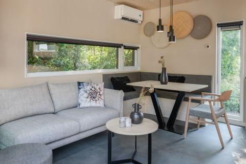 Moderne stue på lodge Noordzee Résidence De Banjaard 23 i Holland med grå sofa og stort vindue.