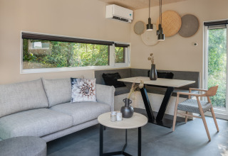 Moderne stue på lodge Noordzee Résidence De Banjaard 23 i Holland med grå sofa og stort vindue.