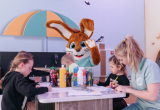 Children and adult crafting with a bunny mascot at a table inside a family-friendly glamping accommodation.