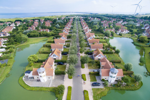 Aerial view of a luxury glamping accommodation with cottages, ponds, green spaces, and wind turbines nearby.
