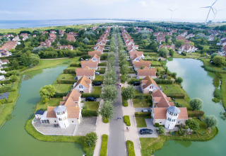 Aerial view of a luxury glamping accommodation with cottages, ponds, green spaces, and wind turbines nearby.