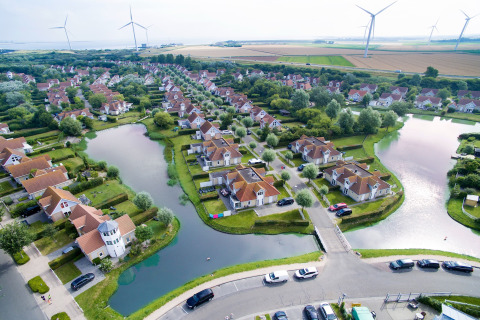 Aerial view of glamping accommodation featuring red roofs, waterways, green landscape, and wind turbines.