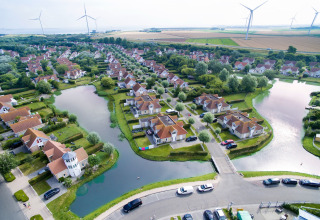 Aerial view of glamping accommodation featuring red roofs, waterways, green landscape, and wind turbines.
