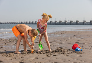 Two children playing with shovels in the sand on the beach, glamping accommodation visible behind.