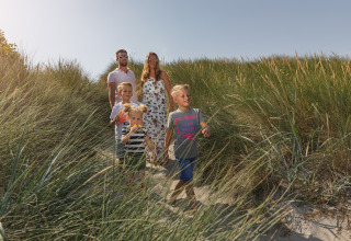 Famille avec trois enfants marchant sur un sentier de plage ensoleillé, hébergement en glamping.