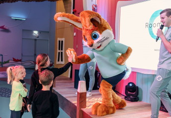 Children interact with a rabbit mascot on stage at a glamping venue while a host speaks on a microphone.