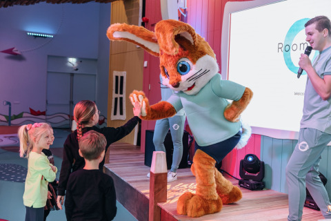 Children interact with a rabbit mascot on stage at a glamping venue while a host speaks on a microphone.