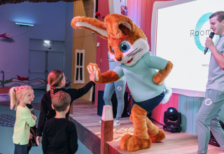 Children interact with a rabbit mascot on stage at a glamping venue while a host speaks on a microphone.
