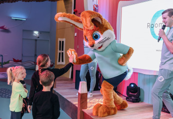 Kinder begrüßen ein Kaninchen-Maskottchen auf einer Bühne bei einer Glamping-Unterkunft mit Moderator.
