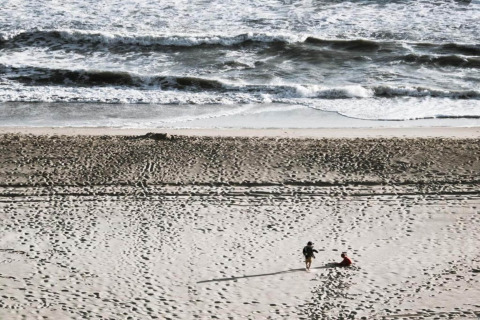 Two people enjoy the sandy beach in front of a glamping site, with waves rolling in the background.