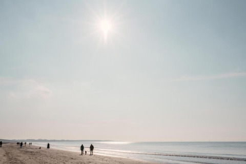 Sunny beach day with people walking by the shoreline, near a glamping accommodation in the distance.