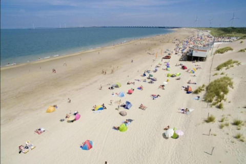 Beach scene at a glamping accommodation with colorful umbrellas and people relaxing in the sun by the sea.