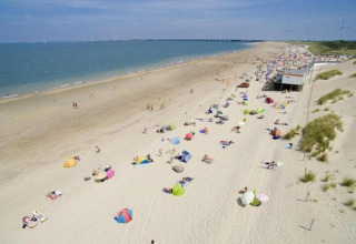 Beach scene at a glamping accommodation with colorful umbrellas and people relaxing in the sun by the sea.