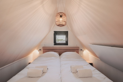 Accogliente camera da letto in tiny house con soffitto inclinato, letto doppio e finestra sopra il letto.