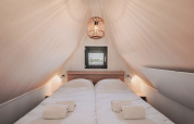 Chambre cosy dans une tiny house avec plafond incliné, lit double, lumière douce et fenêtre au fond.