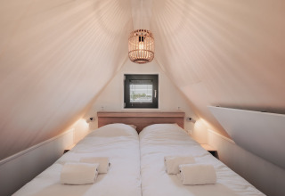 Dormitorio acogedor de tiny house con techo inclinado, cama doble, luz suave y ventana sobre la cama.
