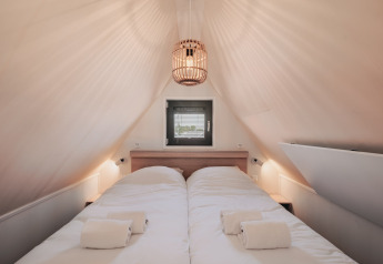 Chambre cosy dans une tiny house avec plafond incliné, lit double, lumière douce et fenêtre au fond.