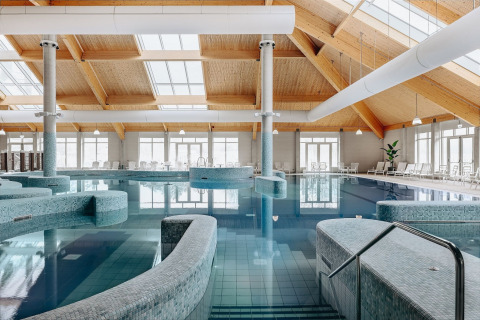Piscina cubierta en un alojamiento glamping, con sillas de descanso y techo de madera con ventanales.