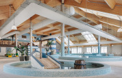 Espace piscine intérieur d’un hébergement glamping avec plafond bois, puits de lumière et toboggan.