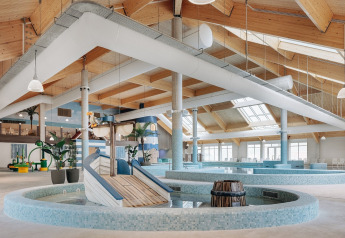 Espace piscine intérieur d’un hébergement glamping avec plafond bois, puits de lumière et toboggan.