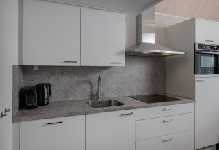 Moderne compacte keuken met witte kasten, kookplaat, oven, dampkap en toestellen in Beach Resort Nieuwvliet-Bad.