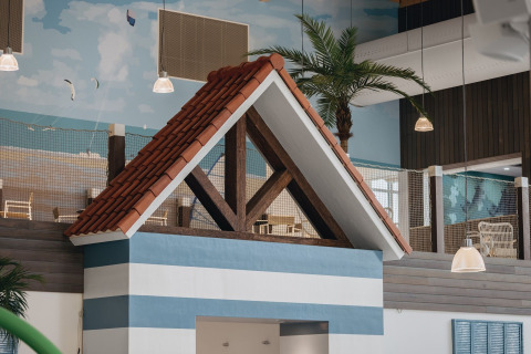 Alojamiento glamping interior con franjas azul y blanco, techo rojo de tejas y palmeras al fondo.