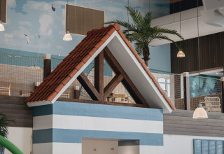 Alojamiento glamping interior con franjas azul y blanco, techo rojo de tejas y palmeras al fondo.