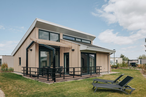 Moderna lodge presso Holiday Park Zeebad 11 con grandi finestre, terrazza e due lettini sul prato verde.