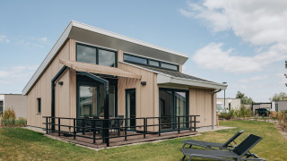 Moderne Lodge im Holiday Park Zeebad 11 mit großer Terrasse, großen Fenstern und zwei Liegestühlen im Garten.