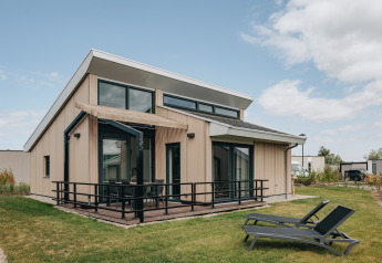 Modern lodge at Holiday Park Zeebad 11 with large windows, deck, and two lounge chairs on the grass lawn.