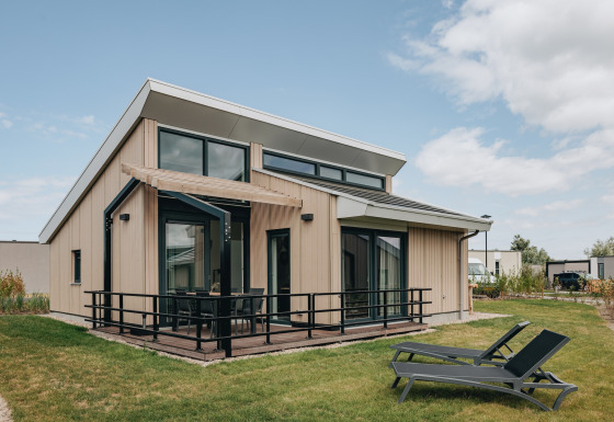 Moderna lodge presso Holiday Park Zeebad 11 con grandi finestre, terrazza e due lettini sul prato verde.