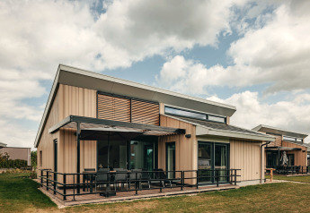 Moderne lodge ved Holiday Park Zeebad 12 med store vinduer, terrasse og naturskønne omgivelser under skyer.