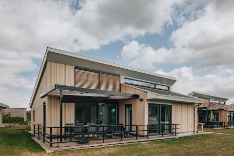 Moderne lodge ved Holiday Park Zeebad 12 med store vinduer, terrasse og naturskønne omgivelser under skyer.