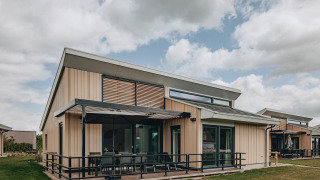 Modern lodge at Holiday Park Zeebad 12 featuring a patio, large windows, and cloudy skies in the background.