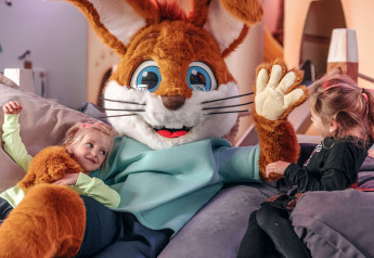 Two children enjoy relaxing with a large bunny mascot in a cozy glamping accommodation setting.