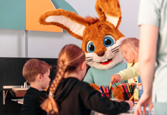 Kinderen knutselen samen met een persoon in een konijnenpak bij een glamping accommodatie.