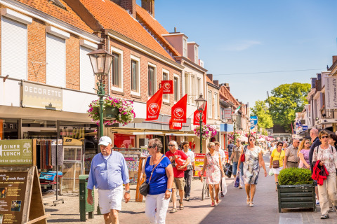 Personas pasean por una animada calle comercial y soleada cerca de un alojamiento de glamping en Holanda.