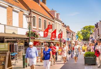 Personas pasean por una animada calle comercial y soleada cerca de un alojamiento de glamping en Holanda.
