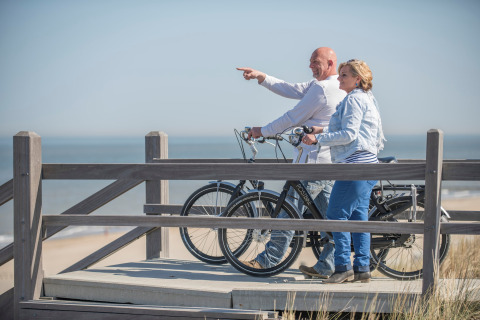 Pareja con bicicletas disfrutando de la vista a la playa desde una terraza de madera en un glamping junto al mar.